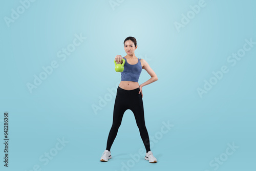 Vigorous energetic woman doing kettlebell weight lifting exercise on isolated background. Young athletic asian woman strength and endurance training session as body workout routine. © Summit Art Creations