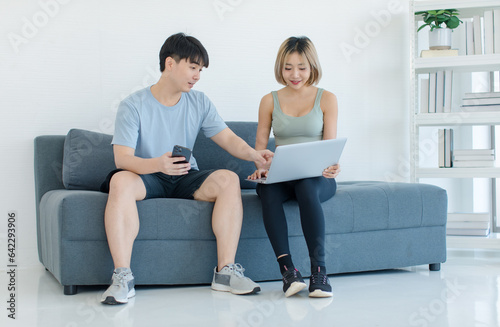 Asian young fit male female husband and wife athlete in sportswear sport bra leggings sneakers sitting on cozy sofa couch learning exercise lesson from laptop notebook computer in living room at home