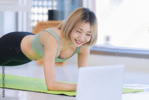 Asian young beautiful female athlete teenager in sportswear sport bra legging stretching body lay down planking on elbows exercising practicing working out abdomen abs on yoga pilates in living room.