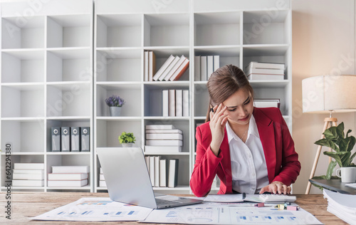 Stressed young Asian businesswoman focuses on rechecking the business financial investment plan's report at her desk. photo