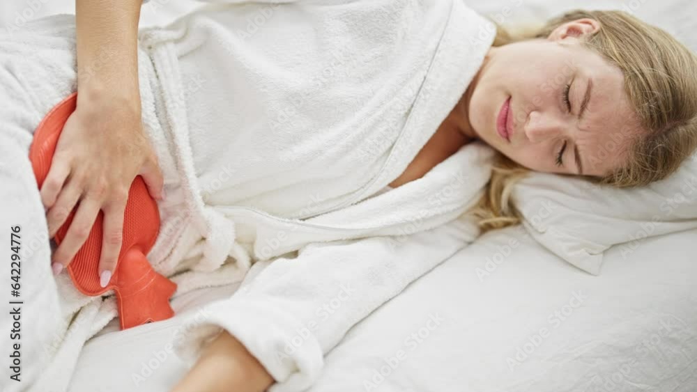 Young blonde woman suffering for menstrual pain lying on bed at bedroom