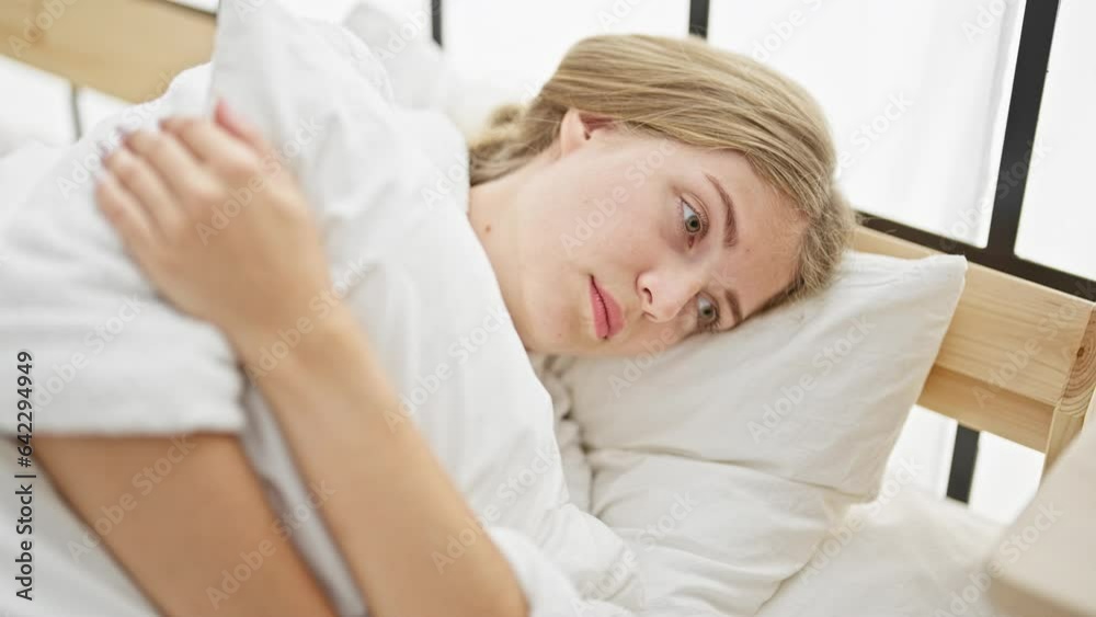 Young blonde woman wearing bathrobe hugging pillow with serious face at bedroom Young blonde woman wearing bathrobe hugging pillow with serious face at bedroom