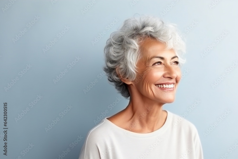 Stylish confident adult 60 years old femal standing smiling looks away at light background. Empty space banner Portrait of sophisticated grey hair woman advertising products and services.
