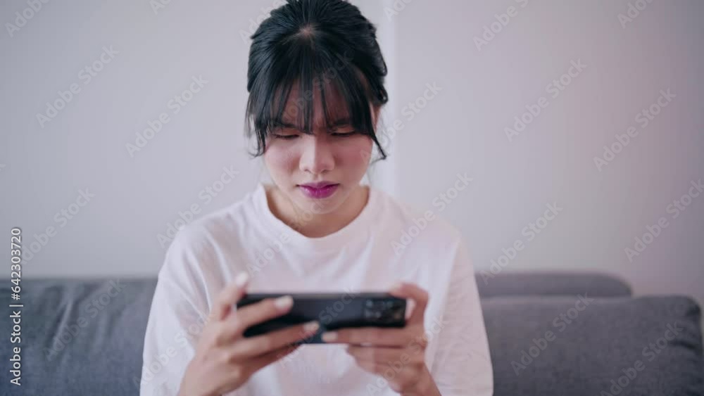 Excited Young Asian woman playing an online game on a smartphone very enjoy and fun relax time at home. Excited Young Asian woman playing an online game on a smartphone very enjoy and fun relax time at home.