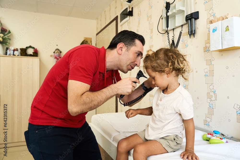 Pediatrician doctor examining child. Male doctor examining boy's ear with otoscope in hospital Pediatrician doctor examining child. Male doctor examining boy's ear with otoscope in hospital