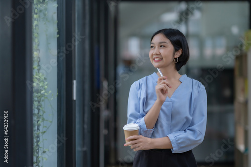 Successful Asian businesswoman smiling standding holding coffee cup at office. photo