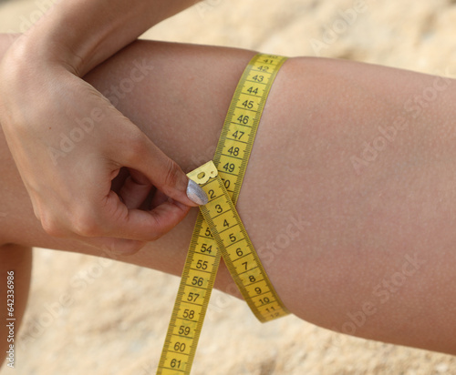 thigh of young woman measured with yellow tape measure and numbers in CENTIMETERS photo