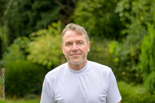 Portrait of a serious and bitter middle-aged man looking at the camera while standing in the garden