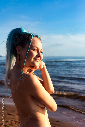 Perfect nude woman posing on nudist sea beach, smiling looking away. Naked slim lady with fashionable hairstyle and sexy body, clothing optional. Nudism naturism lifestyle concept. Copy ad text space