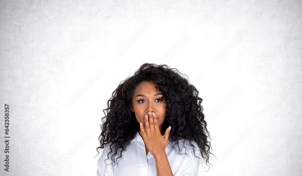 African woman with astonished look, covering her mouth on empty grey background