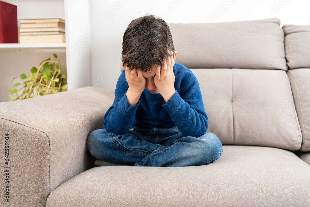 Upset problem child with head in hands sitting on sofa concept for childhood bullying, depression stress or frustration Upset problem child with head in hands sitting on sofa concept for childhood bullying, depression stress or frustration