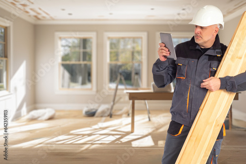 Man builder. Worker with board in his hands. Guy in house under construction. Builder is holding tablet. Worker prepares to wood parquet. Parquet board in hands of builder. Man in brigadier uniform