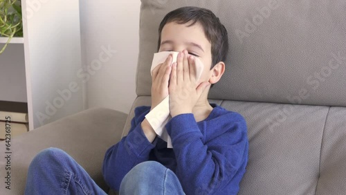 Child blowing in a wipe suffering flu symptoms sitting on a sofa at home in winter photo