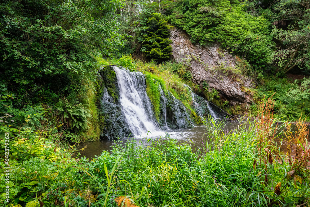 Naklejka premium Crystal clear waterfall surrounded by greenery in the middle of the highlands of Scotland, UK.