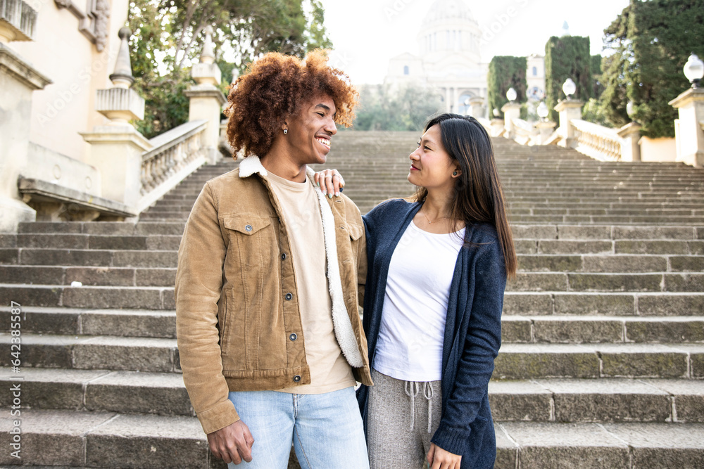Lovely multiracial couple staring at each other in a park.Two happy diverse young persons smiling and looking at each other outside.