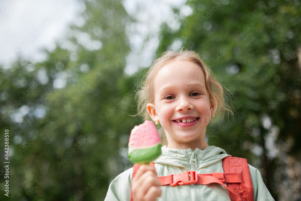 Girl with backpack standing near grassy field and enjoying ice cream Girl with backpack standing near grassy field and enjoying ice cream