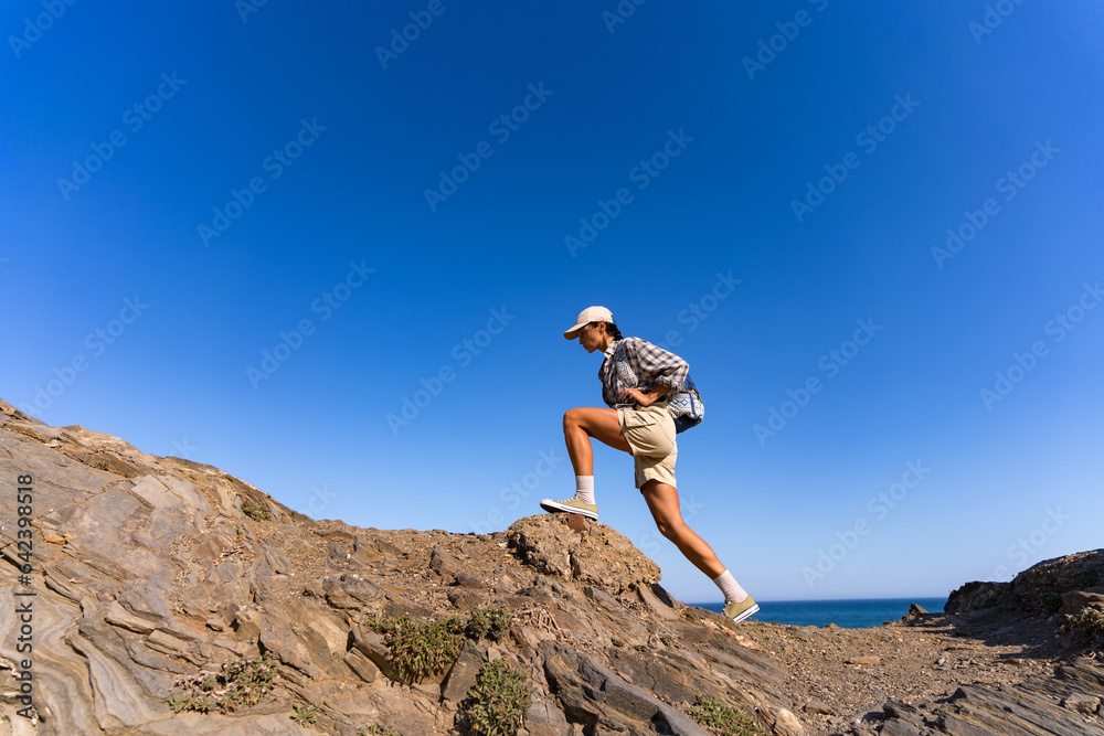 tourist girl with a backpack on her back climbs the mountain in summer