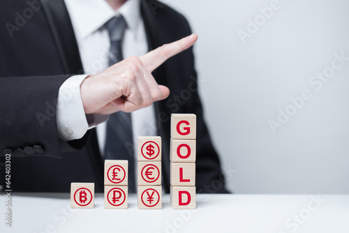 Word gold and red currency icons on wooden blocks: euro, us dollar, bitcoin. Businessman pointing up. Gold, valuable metall, business concept