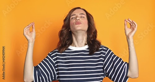 Cheerful young woman enjoying good smell or pleasant fragrance, feel calm breathe fresh air managing stress practicing exercises, peaceful woman. Short curly brunette with woman on yellow background.