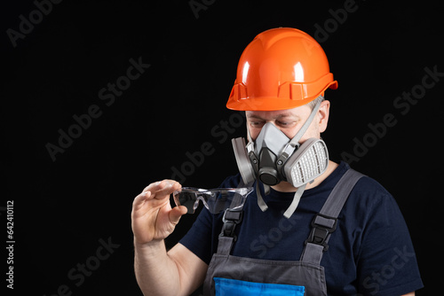 A man wearing a helmet, respirator and goggles on a black background