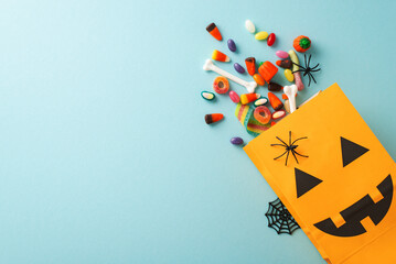 Experience magic of kids' Halloween treat tradition. Top-view shot featuring pumpkin basket, sweets and Halloween decorations on an blue isolated surface, suitable for text or promotional material