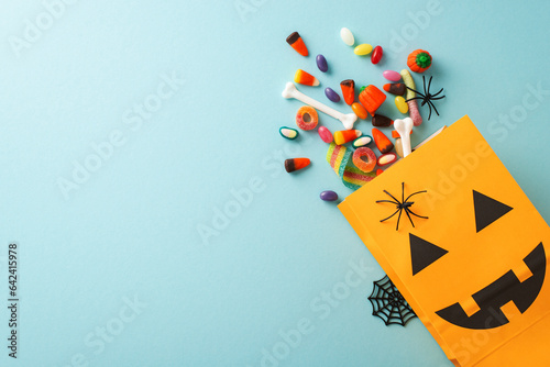 Experience magic of kids' Halloween treat tradition. Top-view shot featuring pumpkin basket, sweets and Halloween decorations on an blue isolated surface, suitable for text or promotional material