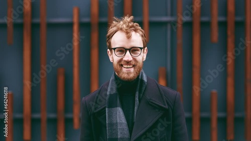 A young red-haired guy, a businessman in glasses, looks at the camera against the background of an urban style. Close up portrait
