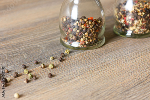 Peas of multi-colored peppers and glass pepper shakers are scattered on a wooden table.