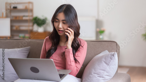 Women talking on smartphone and typing business data on laptop while working in lifestyle at home