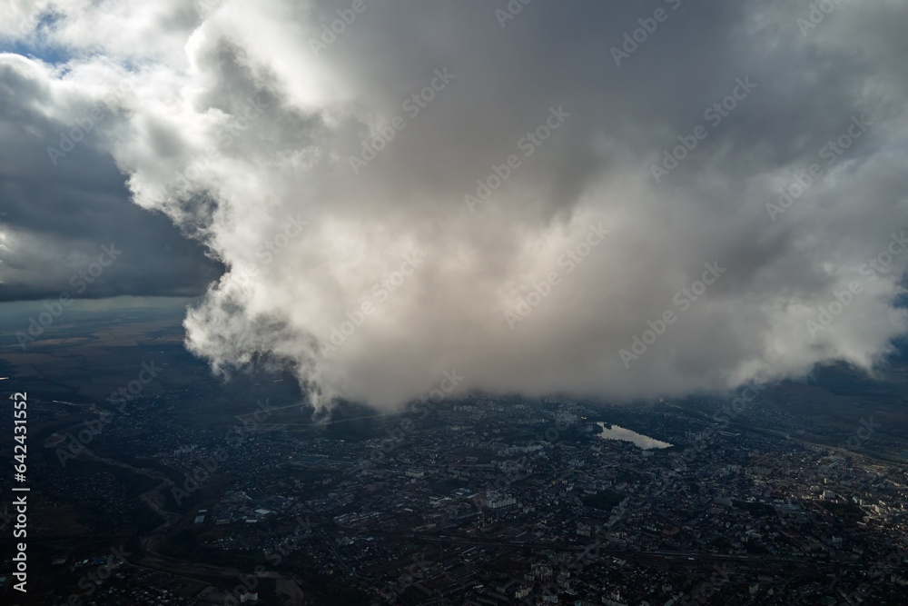 Aerial view from airplane window at high altitude of distant city covered with white puffy cumulus clouds