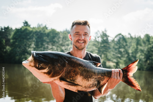 Fishing backgrounds. Happy fisherman hold big trophy fish near lake. Success pike fishing. Fresh fish trophy in hands. Young man returning with freshly caught fish. Article about fishing day. Closeup.