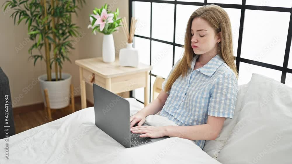 Young blonde woman using laptop sitting on bed looking upset at bedroom Young blonde woman using laptop sitting on bed looking upset at bedroom
