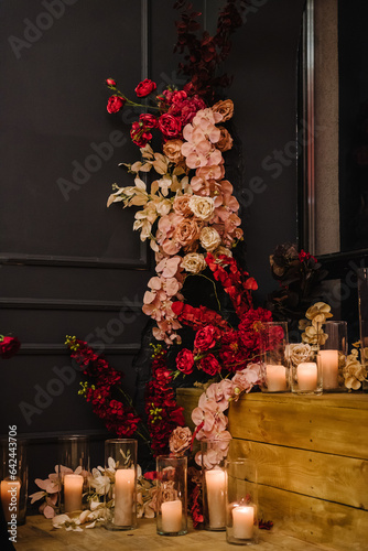 Romantic date in restaurant. Luxury candlelight setup decor for couple on Valentine's day. Location with arch, wall, photo zone decoration flowers, decor with candles for surprise marriage proposal.