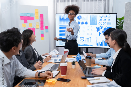 Young african businesswoman presenting data analysis dashboard on TV screen in modern meeting. Business presentation with group of business people in conference room. Concord