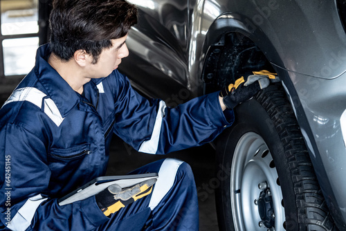 Tyre service and car suspension system maintenance for safety driving. Asian auto mechanic man using digital tablet checking car wheel and rubber tire tread in auto repair shop