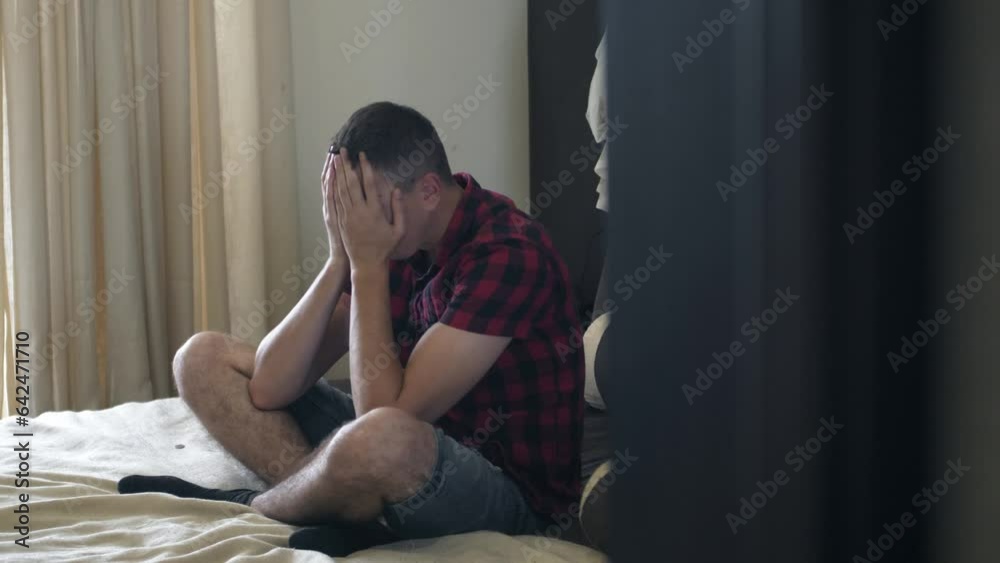 Portrait of upset millennial young man sitting on a bed. Frustrated sad man thinking about something Portrait of upset millennial young man sitting on a bed. Frustrated sad man thinking about something