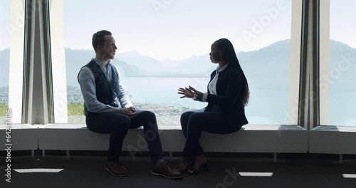 Two young business people talking together inside modern office lobby 