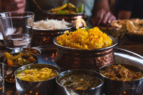 Family eating traditional food in an Indian restaurant. Vegetarian Thali set on the tray, chcken curry, rice, naan and other delicious dishes on the table. Foodie travel background. 