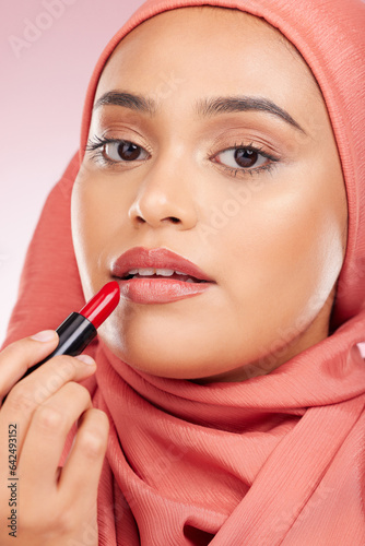Portrait, beauty and lipstick with a muslim woman closeup in studio on a pink background for cosmetics. Face, makeup and islamic with a young model in an hijab to apply a product for red color
