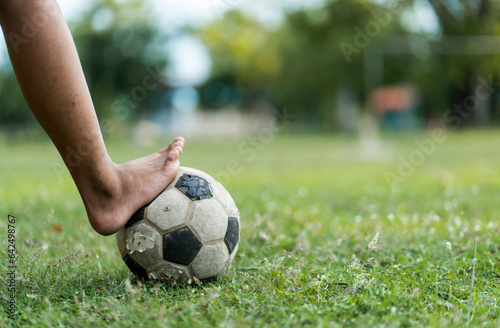 Close up of a old soccer, boy not wearing shoes ready to kicks the ball at the old football field. © khunnok studio
