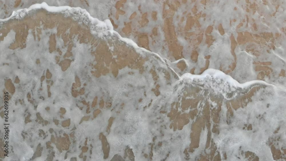 Top aerial view of ocean foam waves rolling on sand beach at tropical beach. Close up Top aerial view of ocean foam waves rolling on sand beach at tropical beach. Close up