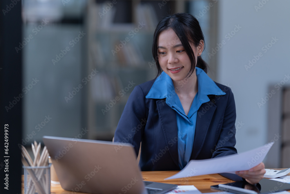 Smiling female browsing laptop and tablet sitting at table with papers and books while in the office. Smiling female browsing laptop and tablet sitting at table with papers and books while in the office.
