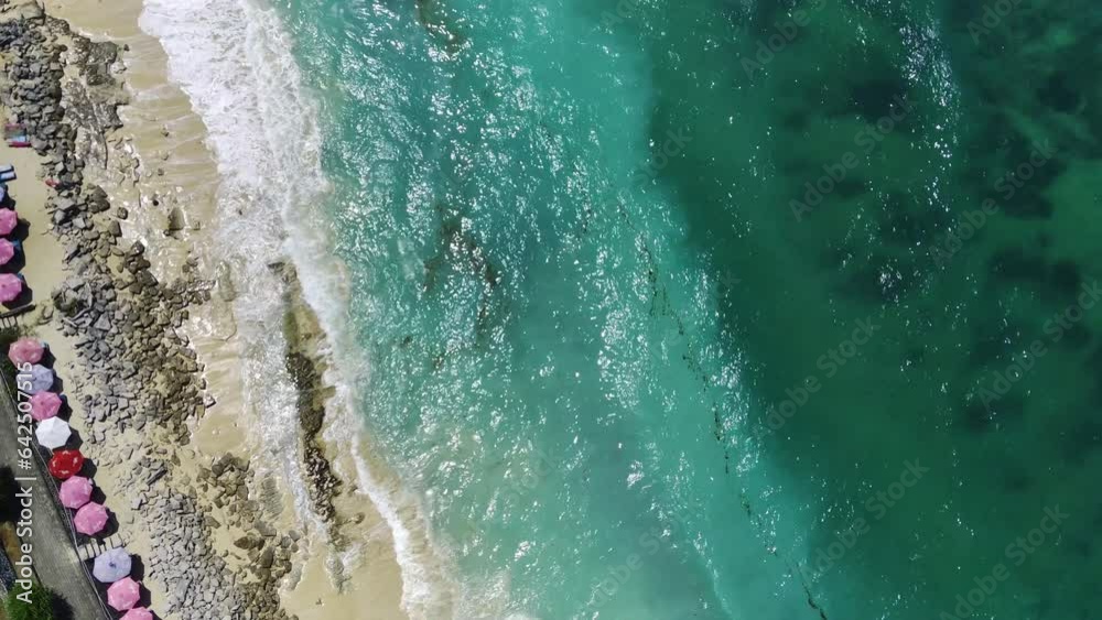 Viewed from the air, the gentle lapping of turquoise colored crystal clear ocean waves washes over the soft white sandy shores, caressing the rocky coastline. Aerial footage taken with drone. Viewed from the air, the gentle lapping of turquoise colored crystal clear ocean waves washes over the soft white sandy shores, caressing the rocky coastline. Aerial footage taken with drone.