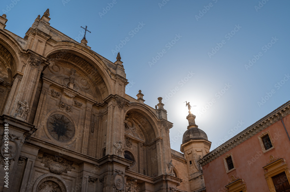 View of the Granada Cathedral with the sun's rays behind the statue of the archangel Saint Michael wielding a sword in one of its domes
