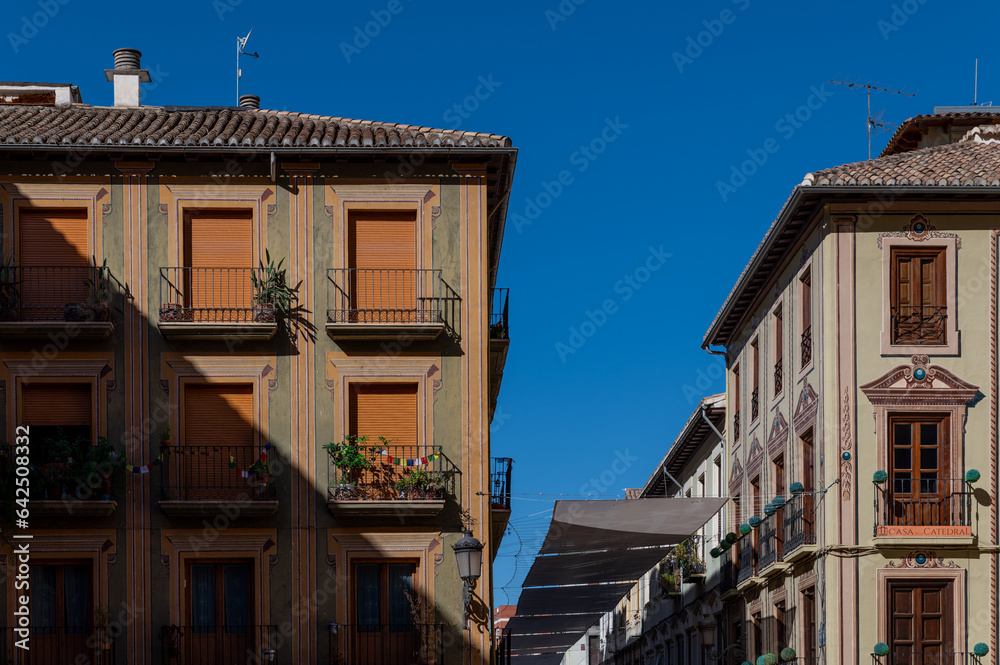 Facade of two old buildings with awnings over the street between them, in Granada (Spain) on a summer morning