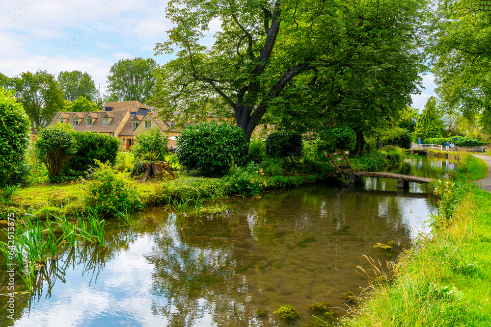 The narrow River Eye as it runs past cottages and homes in the rural Cotswold District at the picturesque village of Lower Slaughter, Cheltenham, Gloucestershire, England, UK.