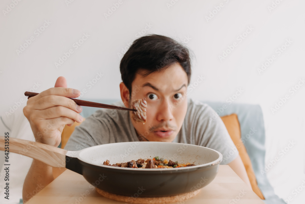 Happy funny face of asian man eating homemade food in the pan with chopsticks. Happy funny face of asian man eating homemade food in the pan with chopsticks.