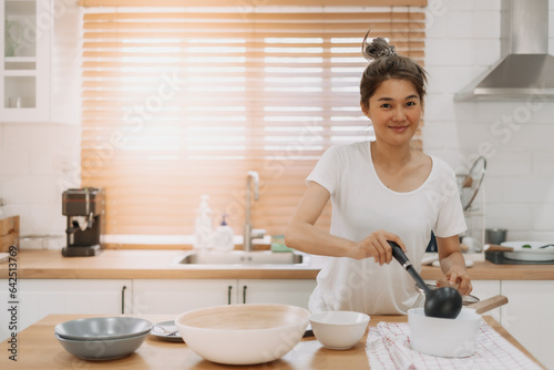 Happy asian woman serving soup into the small bowl.