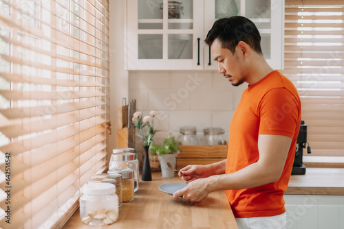 Asian man preparing his easy breakfast in the kitchen in warm light morning.