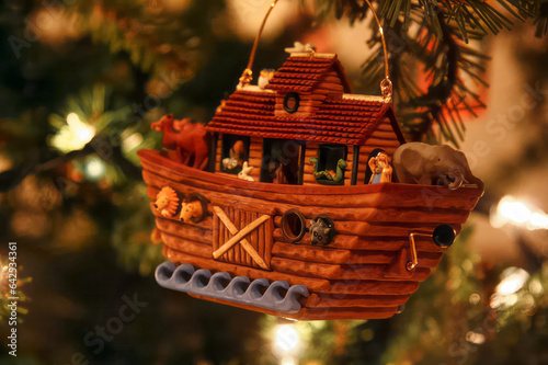 A Noah's Ark Christmas ornament hanging on a Christmas tree. The ship has animals on it, and the atmosphere is warm and festive.